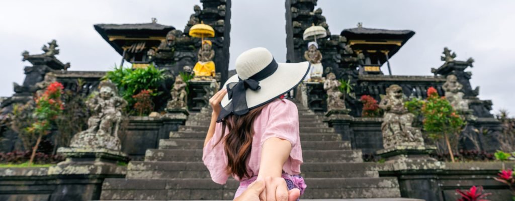 Women tourists holding man's hand and leading him to Besakih temple in Bali, Indonesia.