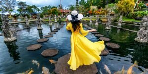 Woman standing in pond with colorful fish at Tirta Gangga Water Palace in Bali, Indonesia.